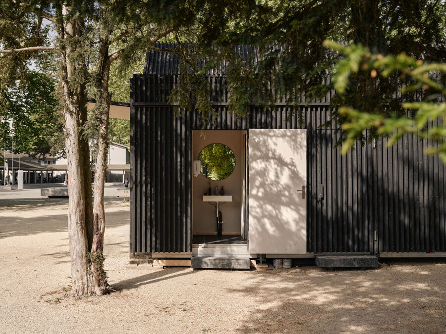 Architekturfotografie: Menschen sitzen und stehen bei der Buvette volAare am Kreuzackerplatz in Solothurn, einer temporären modularen Gastronomie am Aareufer.