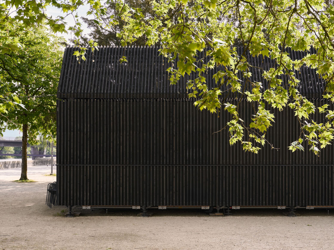 Architekturfotografie: Menschen sitzen und stehen bei der Buvette volAare am Kreuzackerplatz in Solothurn, einer temporären modularen Gastronomie am Aareufer.