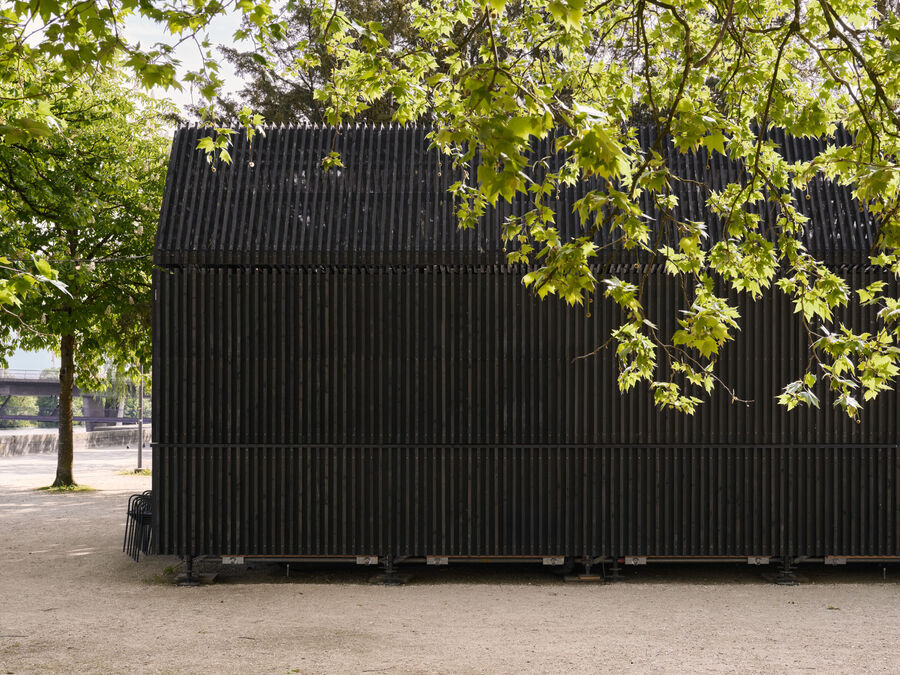 Architekturfotografie: Menschen sitzen und stehen bei der Buvette volAare am Kreuzackerplatz in Solothurn, einer temporären modularen Gastronomie am Aareufer.